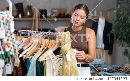 Young woman comes to boutique and looks at clothes Young woman comes to boutique and looks at clothes 135341295