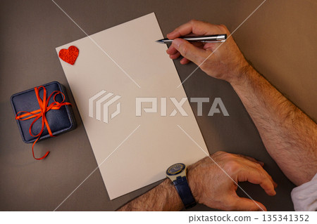 Man writing a romantic letter on blank paper with gift box and heart. Man writing a romantic letter on blank paper with gift box and heart. 135341352