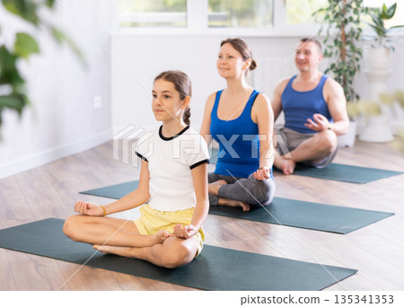 Pleasant preteen girl practicing lotus pose of yoga with her family 135341353