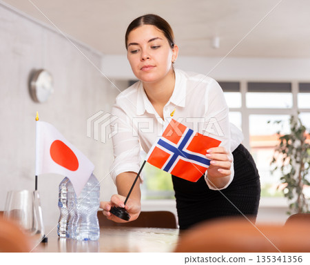 Woman secretary prepares an office for negotiations - she places flags of China and Norway table Woman secretary prepares an office for negotiations - she places flags of China and Norway table 135341356