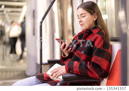 Girl sit in subway car with smartphone, getting to work Girl sit in subway car with smartphone, getting to work 135341357