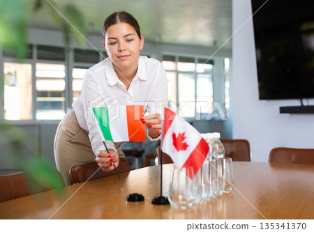 Positive young woman putting little flag of Italy on table next to the flag of Canada 135341370