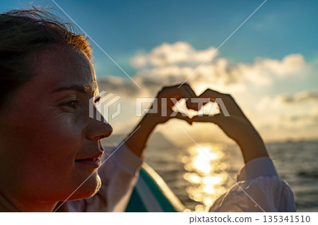 Woman hands heart symbol golden sunset over calm water expressing love and happiness Woman hands heart symbol golden sunset over calm water expressing love and happiness 135341510