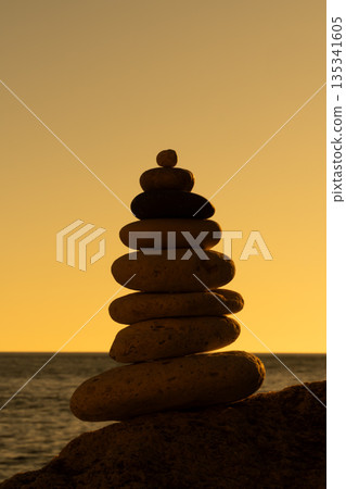 Cairn stones balance, serenity, stack of smooth pebbles on a dark seaside rock during golden sunset with copy space 135341605