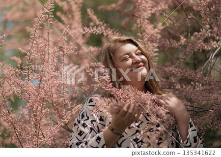 Woman tamarix pink flowers smiling mature lady enjoying soft sunlight among blooming branches Woman tamarix pink flowers smiling mature lady enjoying soft sunlight among blooming branches 135341622