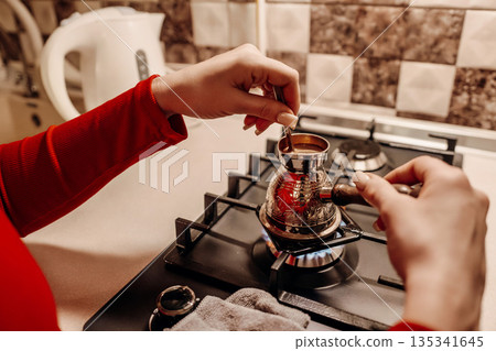 Coffee Brewing Turkey Stovetop Kitchen: Woman prepares traditional coffee on gas stove. 135341645