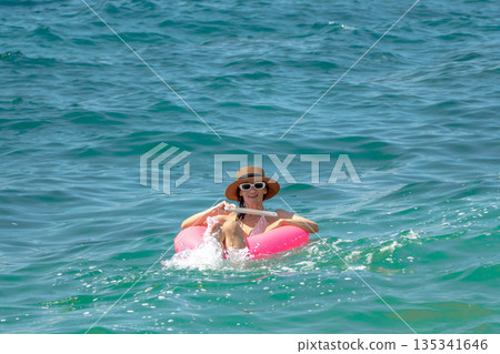 Woman ocean swimming ring splashing water while floating happily on a pink inner tube during summer vacation 135341646