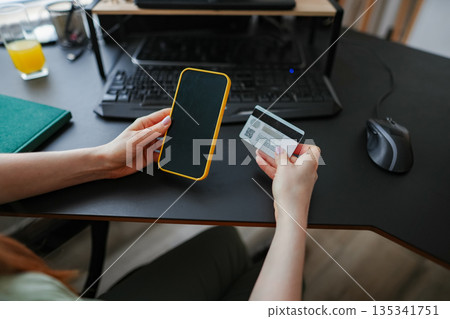 Holding a smartphone and credit card at a modern workspace 135341751