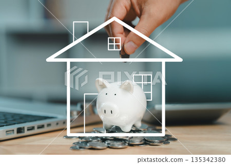 A hand dropping a coin into a piggy bank encased in a white line-art outline of a house, symbolizing the concept of saving money for a home purchase or mortgage. A hand dropping a coin into a piggy bank encased in a white line-art outline of a house, symbolizing the concept of saving money for a home purchase or mortgage. 135342380