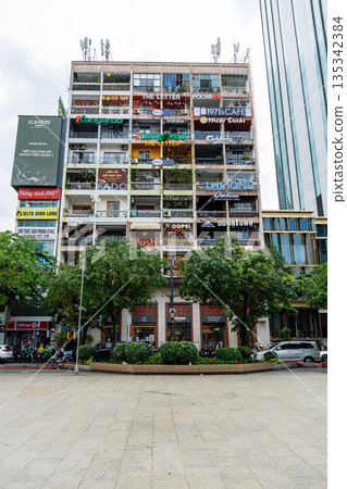 Ho Chi Minh City, Vietnam - June 24, 2025: A vertical shot of a bustling old apartment building in Ho Chi Minh City, Vietnam, with balconies converted into numerous colorful cafes. 135342384