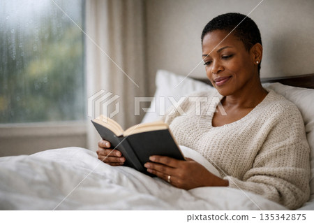 AI generated cozy lifestyle image of a mature black woman reading a book in bed on a rainy afternoon with soft natural light calm mood and comfortable home atmosphere AI generated cozy lifestyle image of a mature black woman reading a book in bed on a rainy afternoon with soft natural light calm mood and comfortable home atmosphere 135342875