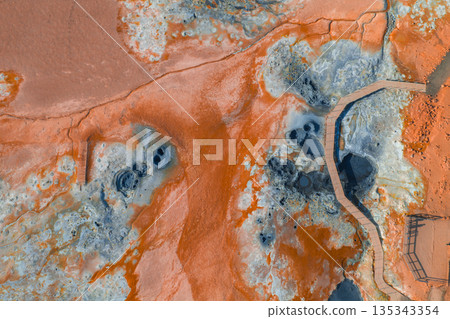 Geothermal area in Iceland with vibrant orange and blue hues, bubbling mud pots, steaming vents, rugged terrain, and a wooden boardwalk for visitors. Geothermal area in Iceland with vibrant orange and blue hues, bubbling mud pots, steaming vents, rugged terrain, and a wooden boardwalk for visitors. 135343354