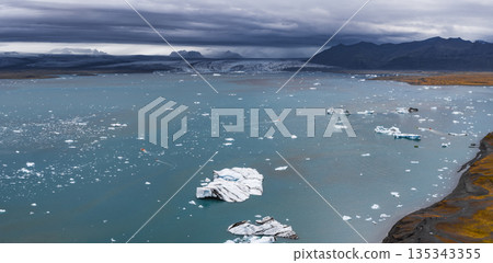 Turquoise waters of Jokulsarlon Glacier Lagoon with floating icebergs, a massive glacier, and dark mountains under a cloudy Icelandic sky. Turquoise waters of Jokulsarlon Glacier Lagoon with floating icebergs, a massive glacier, and dark mountains under a cloudy Icelandic sky. 135343355