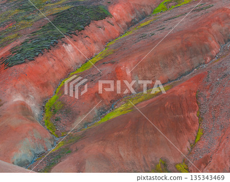 The Rainbow Mountains in Iceland display red, orange, and green hues, with moss and vegetation contrasting against the mineral rich terrain. The Rainbow Mountains in Iceland display red, orange, and green hues, with moss and vegetation contrasting against the mineral rich terrain. 135343469