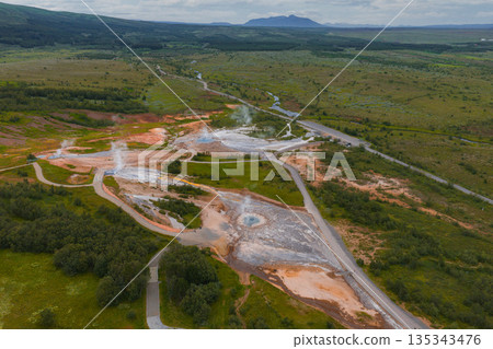 Aerial view of a geothermal area in Iceland with steaming geysers, bubbling hot springs, orange and white mineral deposits, and a meandering river. Aerial view of a geothermal area in Iceland with steaming geysers, bubbling hot springs, orange and white mineral deposits, and a meandering river. 135343476