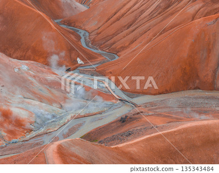 Rust colored rhyolite hills with steam vents, a winding stream, and wooden walkways in the Kerlingarfjoll geothermal area of Iceland. 135343484