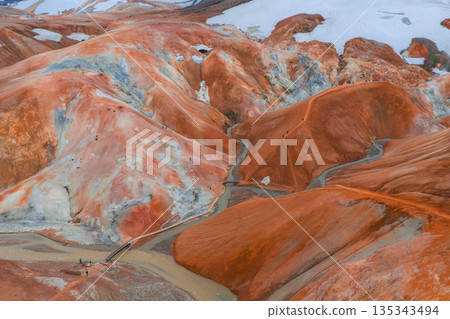 Vibrant rhyolite hills of Kerlingarfjoll in Iceland with orange, red, and yellow hues, steam vents, snow patches, a wooden bridge, and pathways. 135343494