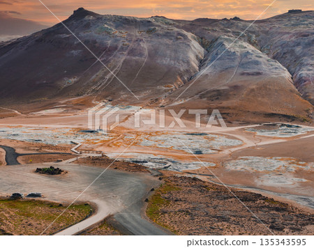Hverir geothermal area near Lake Myvatn, Iceland, features steaming fumaroles, bubbling mud pots, mineral streaked earth, and sunset lit hills. 135343595