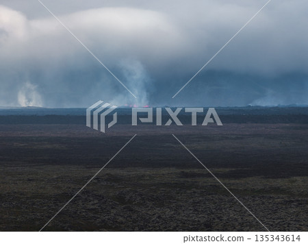 Volcanic eruption in Iceland with glowing red lava, thick smoke, and a rocky foreground. Dense clouds dominate the background, creating a dramatic scene. Volcanic eruption in Iceland with glowing red lava, thick smoke, and a rocky foreground. Dense clouds dominate the background, creating a dramatic scene. 135343614