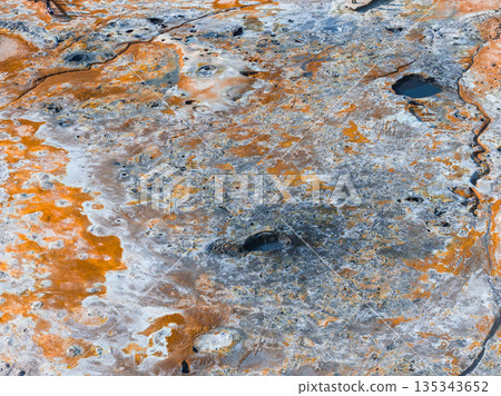 Geothermal landscape in Iceland featuring orange, rust, and gray hues, bubbling mud pots, steaming vents, and small water pools in an aerial perspective. Geothermal landscape in Iceland featuring orange, rust, and gray hues, bubbling mud pots, steaming vents, and small water pools in an aerial perspective. 135343652