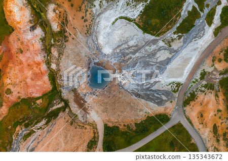 A vivid blue geothermal hot spring surrounded by white and gray mineral deposits, orange and green terrain, and a winding road in Iceland. A vivid blue geothermal hot spring surrounded by white and gray mineral deposits, orange and green terrain, and a winding road in Iceland. 135343672