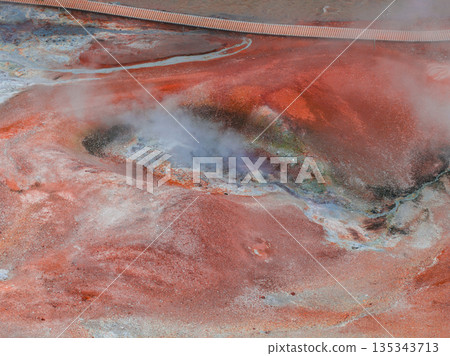 A vibrant geothermal landscape in Iceland with red and orange hues, rising steam, and a visible walkway for exploring the active area. A vibrant geothermal landscape in Iceland with red and orange hues, rising steam, and a visible walkway for exploring the active area. 135343713