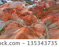 Vibrant rhyolite mountains in Landmannalaugar, Iceland, with red, orange, and brown hues, green moss, snow patches, and a winding river below. 135343735