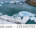 Large icebergs float on turquoise water in Jokulsarlon Glacier Lagoon, Iceland. Patterns of white, blue, and volcanic ash contrast with the rocky shoreline. 135343743