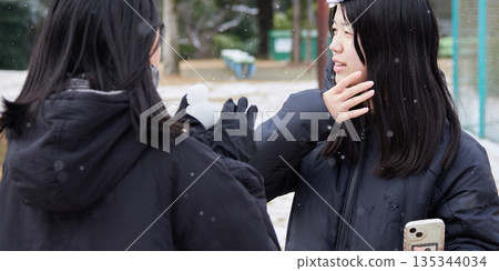 Two little sisters having fun playing a snowball fight in a snowy park on a winter morning 135344034