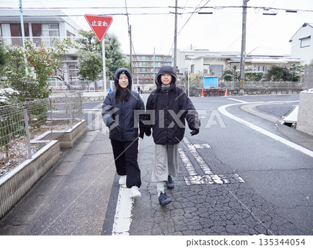 冬日清晨,兩姊妹走在白雪皚皚的居民區。 冬日清晨,兩姊妹走在白雪皚皚的居民區。 135344054