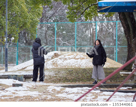 Two little sisters having fun playing a snowball fight in a snowy park on a winter morning Two little sisters having fun playing a snowball fight in a snowy park on a winter morning 135344061