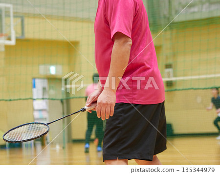 A middle-aged man practicing badminton in a gym A middle-aged man practicing badminton in a gym 135344979