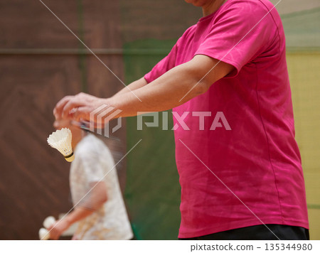 A middle-aged man practicing badminton in a gym A middle-aged man practicing badminton in a gym 135344980