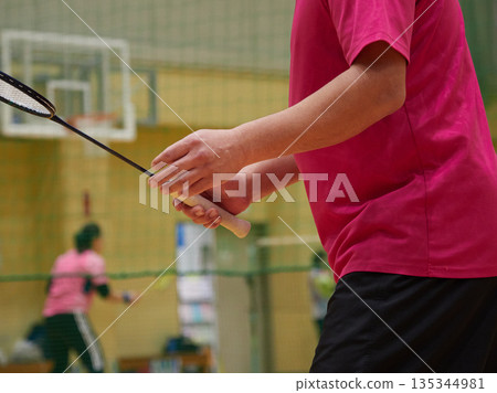 A middle-aged man practicing badminton in a gym A middle-aged man practicing badminton in a gym 135344981