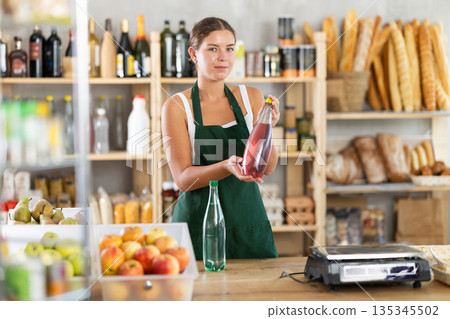 Female salesperson offers to buy a bottle of mineral water in grocery supermarket Female salesperson offers to buy a bottle of mineral water in grocery supermarket 135345502
