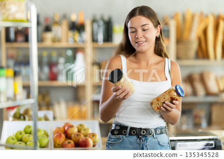Young female shopper carefully choosing jar of canned beans in grocery supermarket 135345528