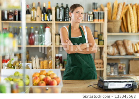 Portrait of smiling female salesperson in apron behind supermarket counter Portrait of smiling female salesperson in apron behind supermarket counter 135345568