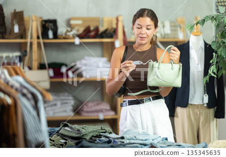 Girl customer choose handbag in store, and buyer carefully examines product. Girl customer choose handbag in store, and buyer carefully examines product. 135345635
