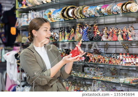 Woman tourist choosing souvenirs while traveling in Spain, looking at handcrafted souvenirs displayed in artisan store Woman tourist choosing souvenirs while traveling in Spain, looking at handcrafted souvenirs displayed in artisan store 135345694