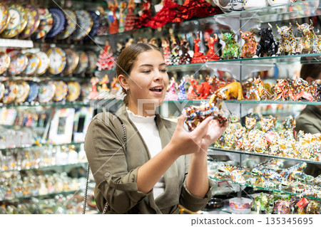 Cheerful female tourist choosing colorful bull statuette at tourist shop 135345695