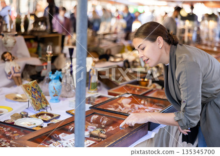 Cheerful female tourist choosing antique jewelry at flea market 135345700
