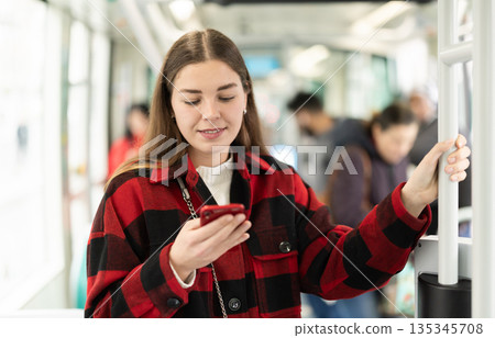 Girl is standing with phone in tram car, getting to work 135345708