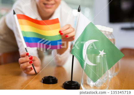 Little flag of Pakistan on table and LGBT flag put next to it by young woman 135345719