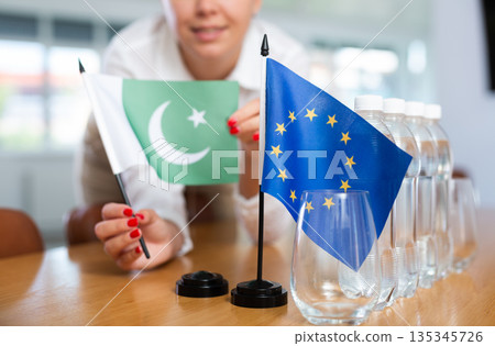 Woman secretary prepares an office for negotiations - she places flags of European Union and Pakistan table Woman secretary prepares an office for negotiations - she places flags of European Union and Pakistan table 135345726