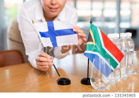 Little flag of South Africa on table and flag of Finland put next to it by young woman Little flag of South Africa on table and flag of Finland put next to it by young woman 135345905