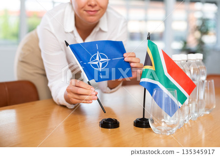 Little flag of South Africa on table and flag of NATO put next to it by young woman 135345917