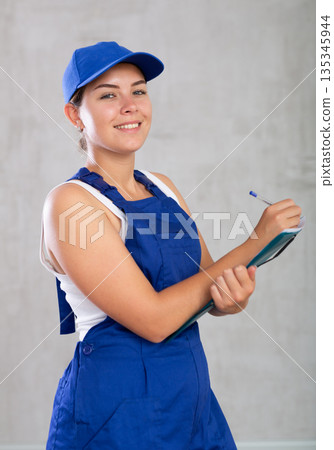 Happy female worker in work clothes making notes in file with papers 135345944