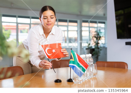 Positive young woman putting little flag of Turkey on table next to the flag of South Africa Positive young woman putting little flag of Turkey on table next to the flag of South Africa 135345964