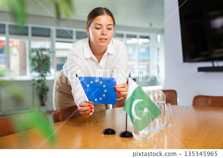 Positive young woman putting little flag of European Union on table next to the flag of Pakistan Positive young woman putting little flag of European Union on table next to the flag of Pakistan 135345965