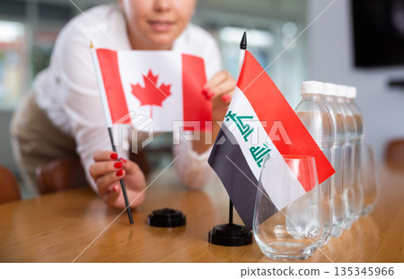 Employee of delegation prepares negotiating table - sets up flag of Canada and Iraq Employee of delegation prepares negotiating table - sets up flag of Canada and Iraq 135345966